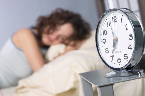 Woman laying down looking at her clock avoiding exercise.