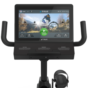 A close-up of the Performance Series Recumbent Bike’s touchscreen shows various cycling workouts, flanked by handlebars and a pedal with foot strap below. The display features an outdoor cycling scene.