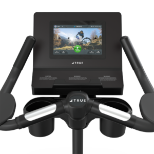 Close-up view of a Performance Series Upright Bike console with a touchscreen display showing a virtual outdoor workout and two cup holders beside the handlebars.